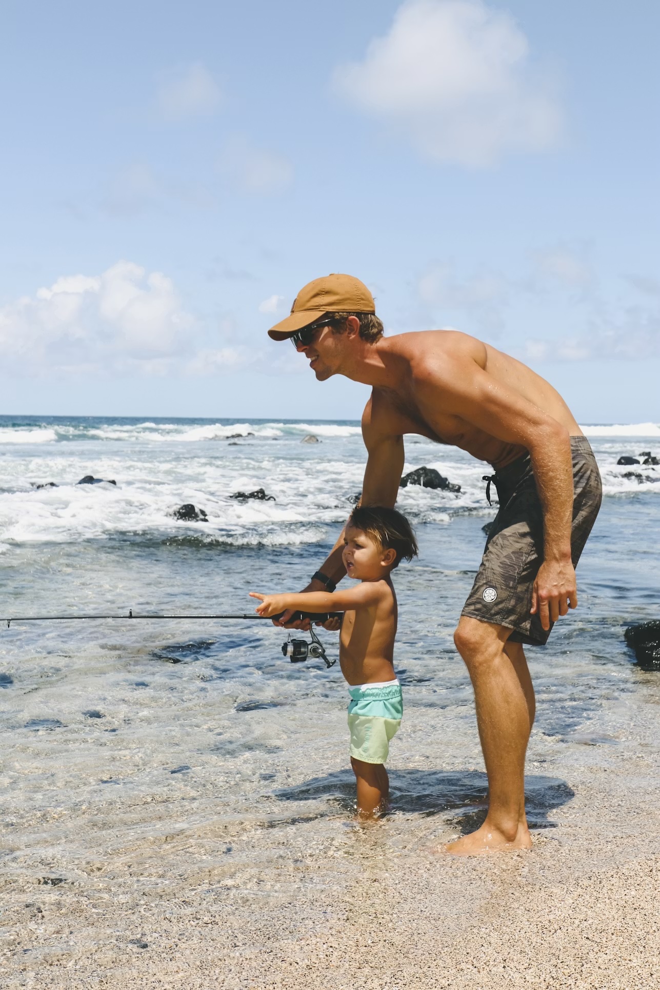A father helping his young son fish at the beach.